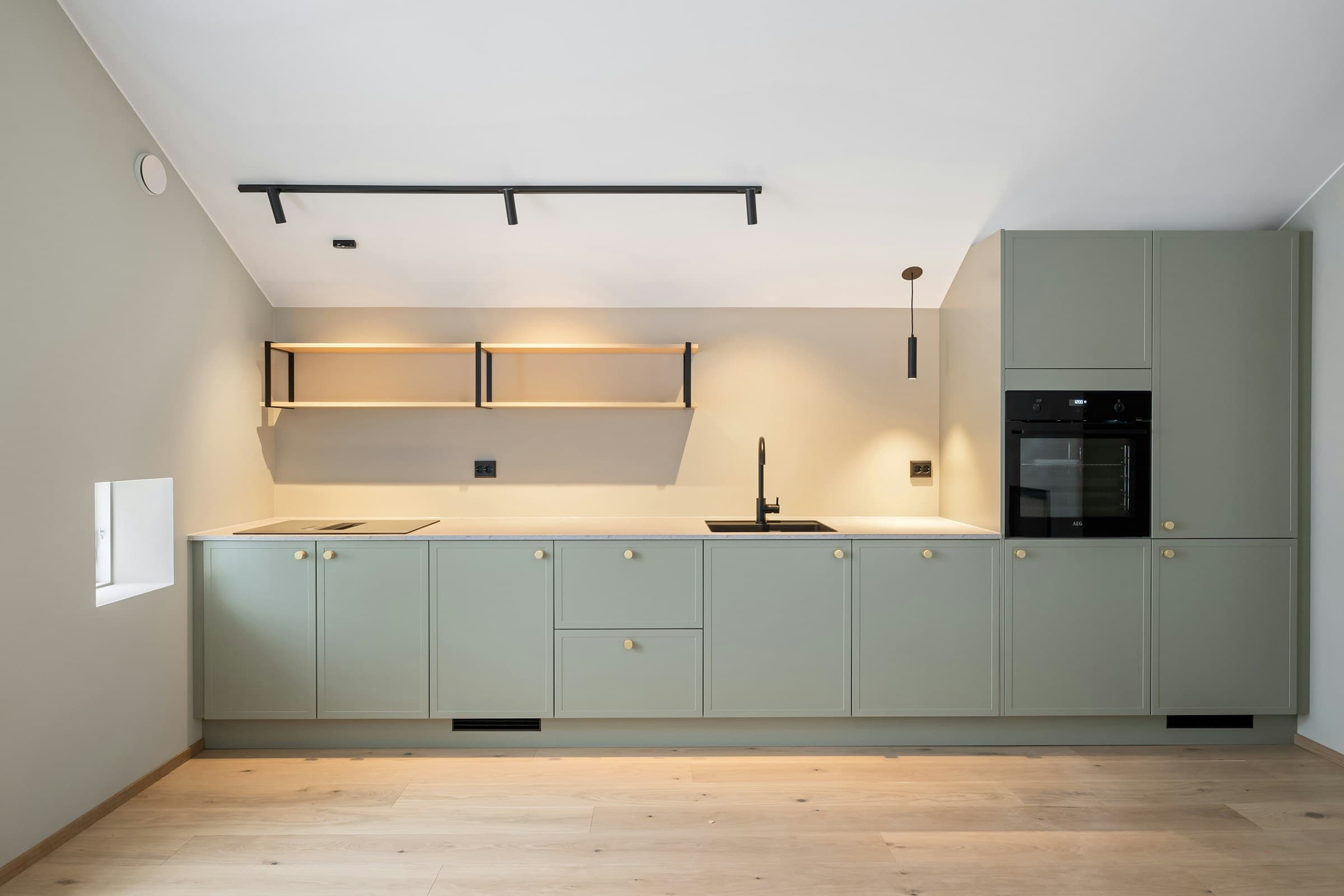 Cocina terminada con muebles verde salvia, tiradores de latón y suelo de madera.