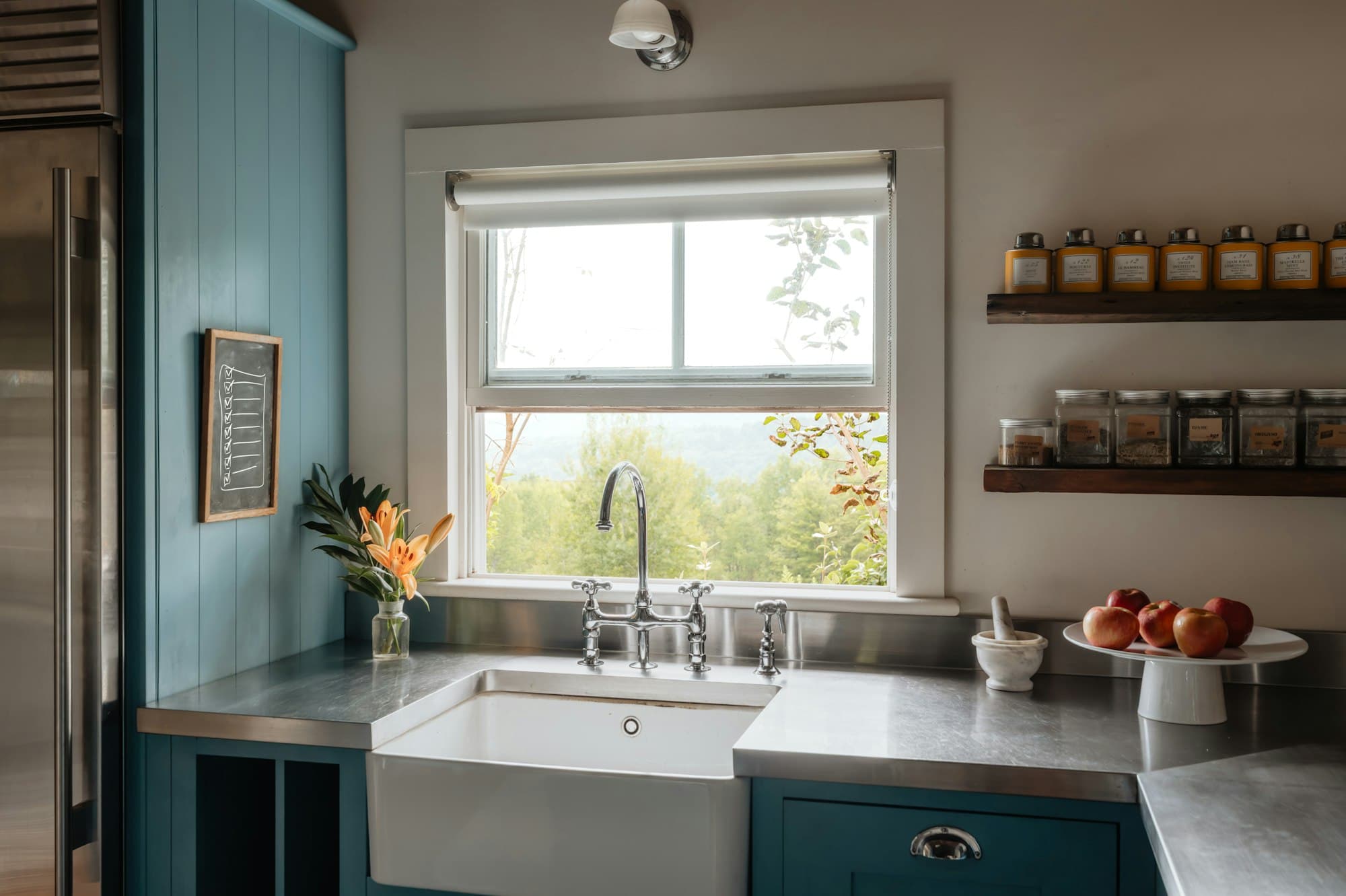 Después: cocina con muebles azul petróleo, encimera de acero y fregadero bajo la ventana.